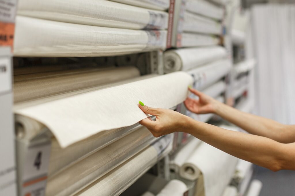 A young woman in a hardware store buys wallpaper. Pulls a roll of wallpaper from the shelf.