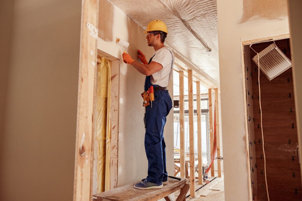 Male builder painting wall in house under construction
