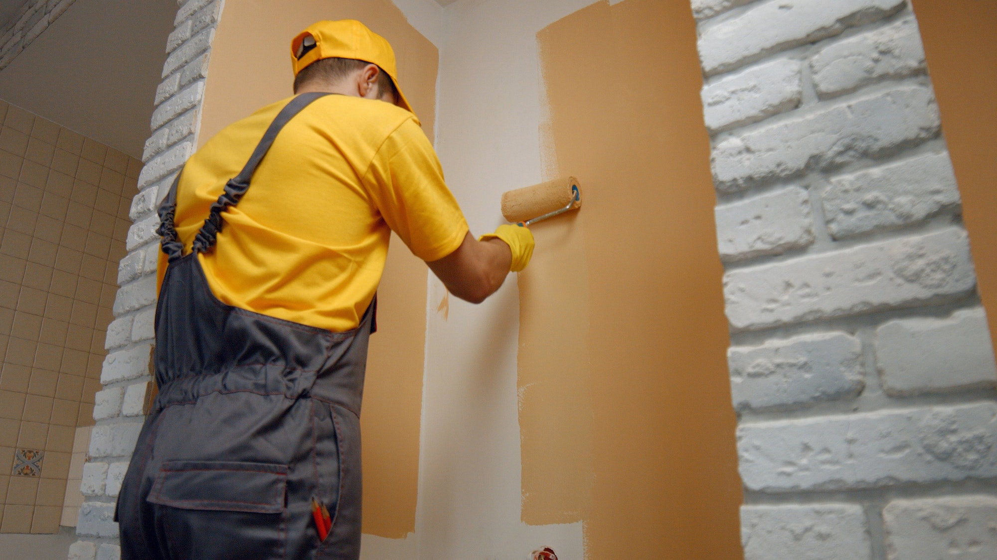 Worker painting wall with paint roller.